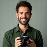 Retrato de Juan Camilo Estrada, Fotógrafo Principal de Colmena Visual, sonriendo con una cámara de macro en mano.
